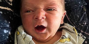 Oliver is registered to the contest to win money with this photo: baby, newborn, infant, face, expression, mickey_mouse, cartoon, shirt, clothing, hand, lying_down, blanket, pattern, cute, child, portrait, skin, indoors, person, closeup