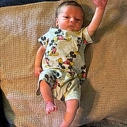 Oliver joined the competition — help win amazing prizes! baby, infant, mickey_mouse, onesie, clothing, towel, fabric, hand, foot, lying_down, raised_arm, expression, skin, person, newborn, cute, indoor, texture, pattern, soft