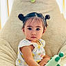 toddler, child, pigtails, toy, bean_bag, plush, indoor, portrait, cute, curious, flower_pattern, clothing, furniture, face, person, young_child, comfortable, natural_light, home, seated