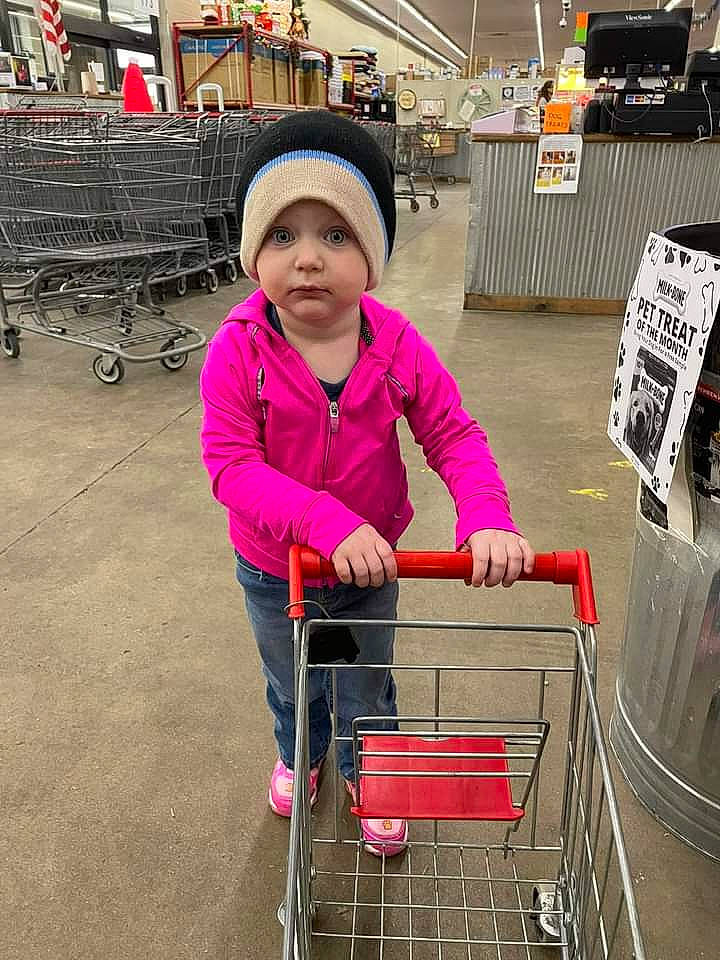 Carley is registered to the contest to win money with this photo: city, customer, fun, headwear, helmet, human, jacket, leisure, magenta, mode_of_transport, motor_vehicle, person, pink, recreation, shopping, shopping_cart, standing, tire, toddler, travel