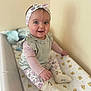 baby, child, smiling, headband, floral, leggings, sitting, changing_table, indoor, cute, happy, person, infant, wall, soft_light, apparel, footwear, pattern, cozy, playful