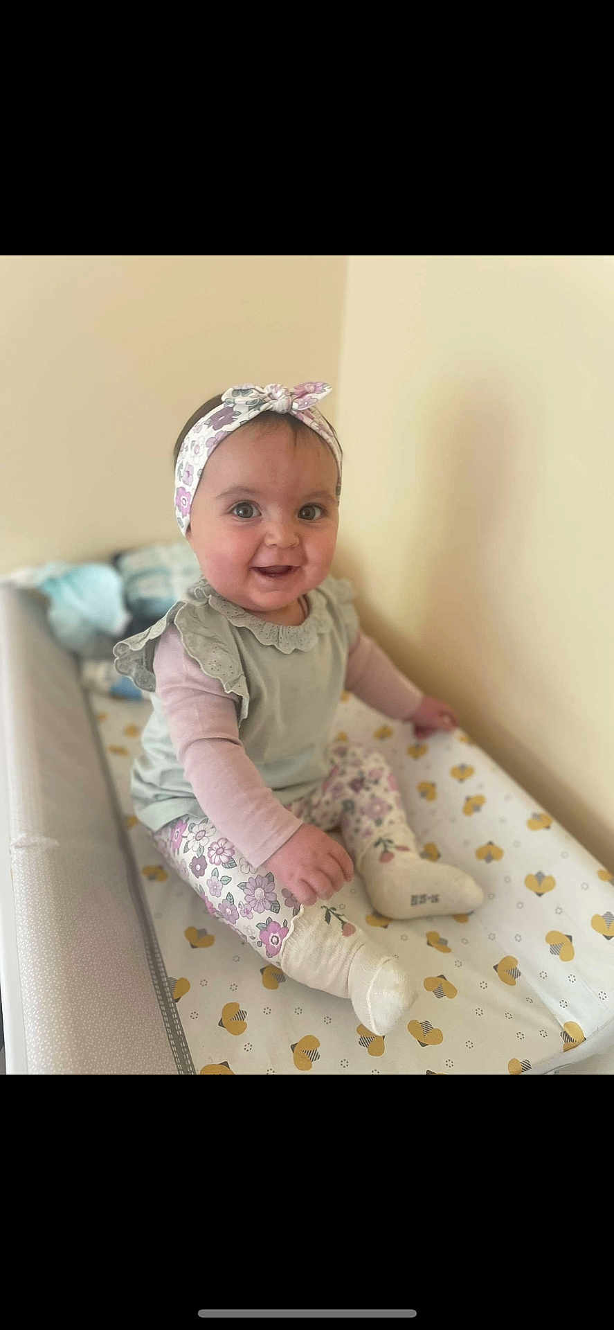 Livia participe au concours pour gagner de l'argent avec cette photo : baby, child, smiling, headband, floral, leggings, sitting, changing_table, indoor, cute, happy, person, infant, wall, soft_light, apparel, footwear, pattern, cozy, playful