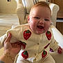baby, child, smiling, laughing, person, indoor, couch, armchair, hand, tattoo, bracelet, knitwear, strawberry_pattern, cozy, home, furniture, pillow, plant, wooden_furniture, floor