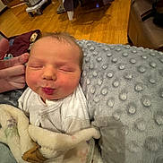 Lehman is registered to the contest to win money with this photo: baby, newborn, blanket, pillow, sleeping, indoor, infant, soft_texture, cozy, person, cute, face, resting, hand, wood_floor, clothing, wrapped, closeup, peaceful, expression