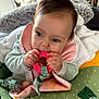 Emy a rejoint le concours — aidez-le/la à gagner de superbes lots ! baby, infant, teething_ring, blanket, pillow, soft_texture, child, cute, indoor, closeup, face, hand, clothing, pink, green, white, playtime, comfort, focus, young