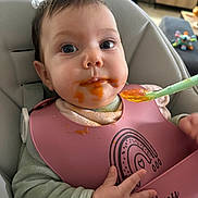 Emy a rejoint le concours — aidez-le/la à gagner de superbes lots ! baby, infant, high_chair, bib, feeding, spoon, food, messy, face, child, indoor, living_room, toy, furniture, person, cute, mouth, clothing, hand, expression