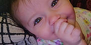 Victoria is registered to the contest to win money with this photo: baby, child, face, smiling, thumb, hand, blanket, clothing, close_up, cute, infant, person, skin, happy, indoors, young, lying_down, soft, portrait, comfort
