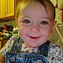 baby, child, smiling, face, denim_overalls, floral_shirt, indoor, kitchen, wooden_cabinets, person, cute, happy, portrait, clothing, infant, closeup, eyes, hair, baby_girl, overalls