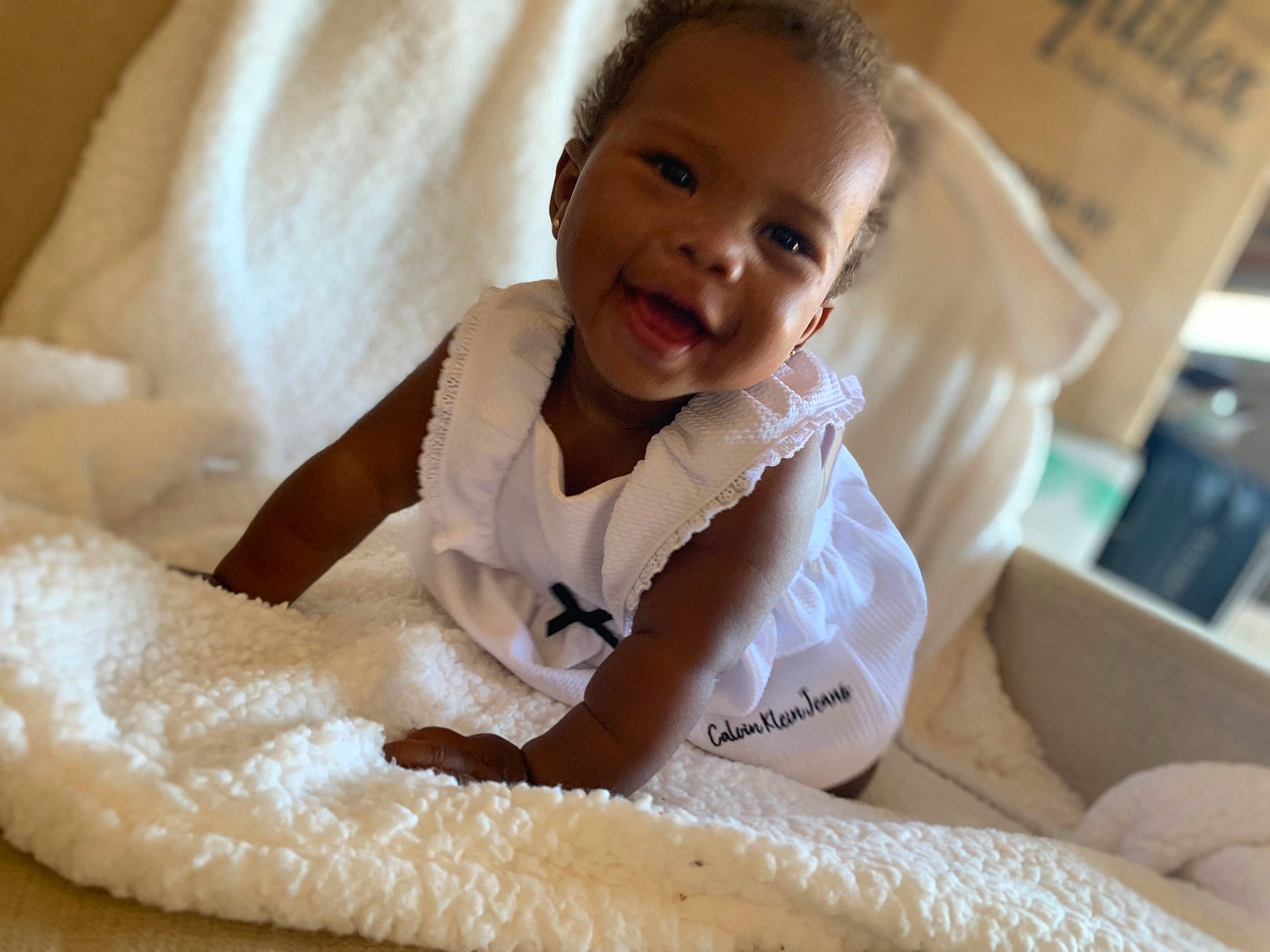 Ariya is registered to the contest to win money with this photo: baby, baby_products, bed_sheet, bedding, blanket, child, comfort, eye, finger, flooring, fur, happy, head, human_leg, linens, neck, person, room, sitting, smile