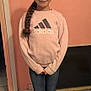 child, girl, braid, standing, pink_wall, adidas_sweatshirt, jeans, sneakers, indoor, floor, drawing, artwork, smile, casual_clothing, portrait, young_person, childhood, happy, hair_tie, pose