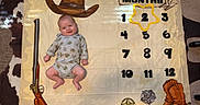 Hayes is registered to the contest to win money with this photo: baby, baby_boy, celebration, child, cowboy_boots, cowboy_hat, cowhide_rug, cute, decor, floor, indoor, infant, lying_down, milestone_blanket, months, onesie, portrait, rifle_illustration, sheriff_badge, smiling