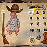 baby, baby_boy, celebration, child, cowboy_boots, cowboy_hat, cowhide_rug, cute, decor, floor, indoor, infant, lying_down, milestone_blanket, months, onesie, portrait, rifle_illustration, sheriff_badge, smiling