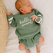 Hayes is registered to the contest to win money with this photo: newborn, baby, infant, sleeping, yawning, knitted_clothing, green_sweater, green_shorts, text_on_clothing, blanket, cushion, soft_texture, cozy, cute, peaceful, lying_down, indoors, portrait, person, child