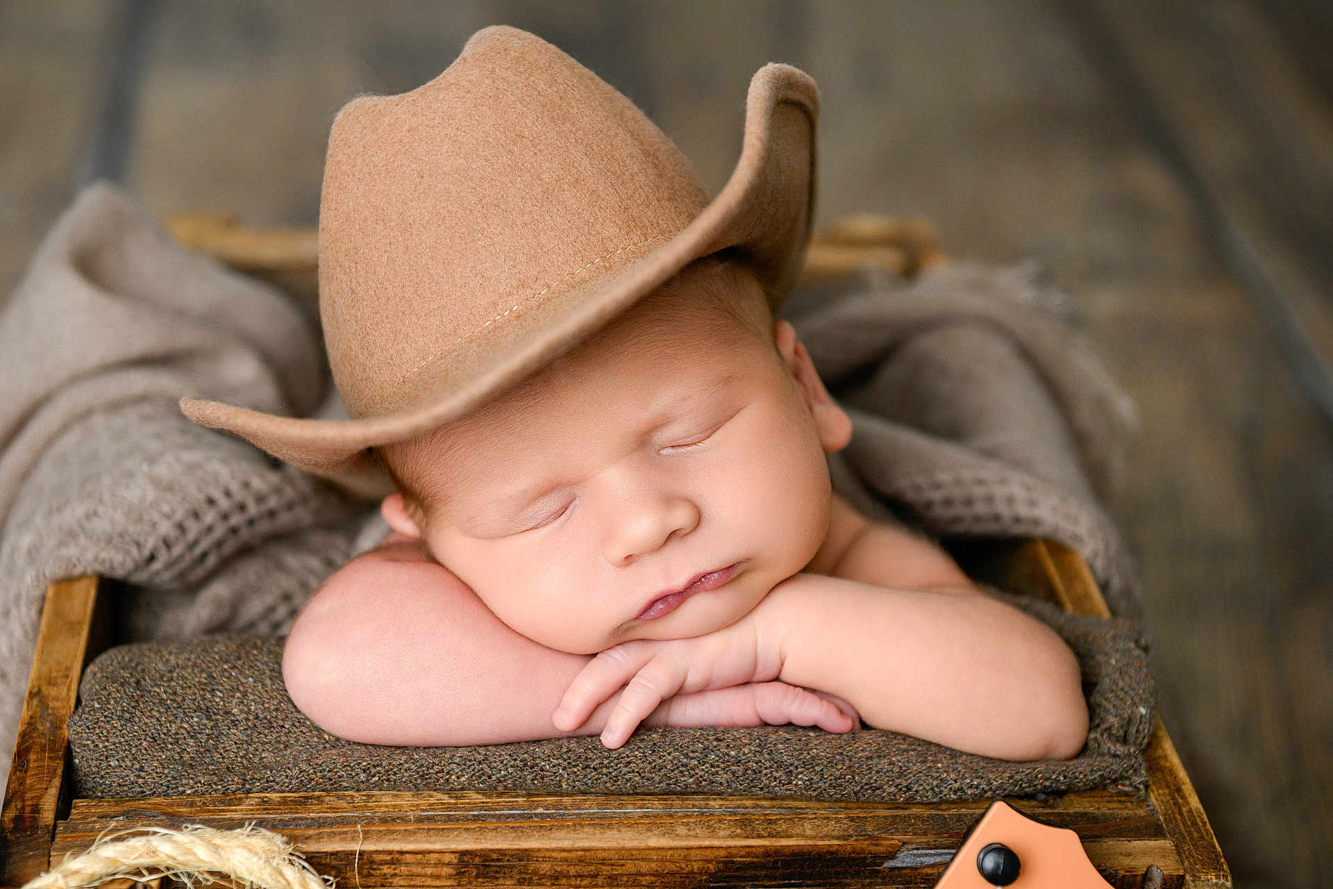 Jackson is registered to the contest to win money with this photo: baby, sleeping, hat, cowboy_hat, resting, arms, blanket, wooden_crate, cozy, soft, face, peaceful, infant, closeup, portrait, indoors, wood_floor, newborn, cute, child
