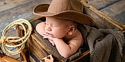 Jackson is registered to the contest to win money with this photo: baby, cowboy_hat, sleeping, wooden_box, blanket, rope, ukulele, arm, face, resting, infant, wood_floor, cozy, child, indoors, cute, napping, hat, small_instrument, peaceful