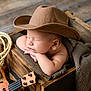 baby, cowboy_hat, sleeping, wooden_box, blanket, rope, ukulele, arm, face, resting, infant, wood_floor, cozy, child, indoors, cute, napping, hat, small_instrument, peaceful