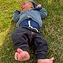baby, infant, grass, outdoor, knitted_sweater, blue_clothing, pants, barefoot, relaxed, sunlight, nature, child, person, casual_wear, greenery, daylight, lying_down, cute, small_child, peaceful