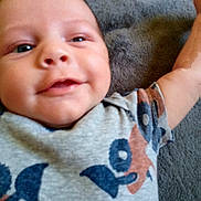 River is registered to the contest to win money with this photo: baby, smiling, face, arm, clothing, pattern, grey_blanket, closeup, infant, cute, happy, skin, person, head, child, young, portrait, lying_down, casual, soft_texture