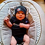 baby, infant, child, champion_brand, black_clothing, hat, onesie, baby_seat, padded_seat, footwear, socks, wooden_floor, indoor, cute, portrait, young_child, apparel, headwear, expression, relaxed