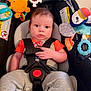 baby, car_seat, child, infant, toy, hanging_toy, blue_eyes, clothing, straps, safety_buckle, indoor, seat, cute, expression, person, face, hand, orange_shirt, gray_pants, plush_toy