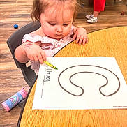 Chesney is registered to the contest to win money with this photo: toddler, child, bow, coloring, worksheet, table, chair, crayon, floor, wood, classroom, kids, shoes, water_bottle, pink, purple, play, learning, young_child, indoor