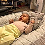 baby, infant, baby_lounger, cushion, star_pattern, clothing, pants, long_sleeve, face, skin, hand, furniture, chair, table, floor, room, indoor, living_room, appliance, blanket