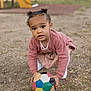 toddler, child, soccer_ball, playground, outdoor, grass, curious, pigtails, pink_cardigan, kneeling, toy, young_child, park, casual_clothing, play, daylight, colorful_ball, ground, recreation, fun