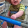 baby, infant, smiling, shopping_cart, supermarket, walmart, child, face, socks, legs, hand, striped_socks, overalls, person, parent_arm, store_shelves, groceries, cart_handle, metal_cart, joyful