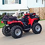 atv, backyard, blurred, daytime, dog, dog_sitting, driveway, fence, four_wheeler, garden, grass, house, nature, outdoor, pet, residential, suburban, vehicle, white_dog, yard