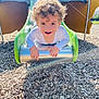 child, toddler, curly_hair, slide, playground, outdoor, wood_chips, happy, smiling, sunlight, shadow, play, fun, clothing, person, daylight, recreation, park, casual_wear, activity