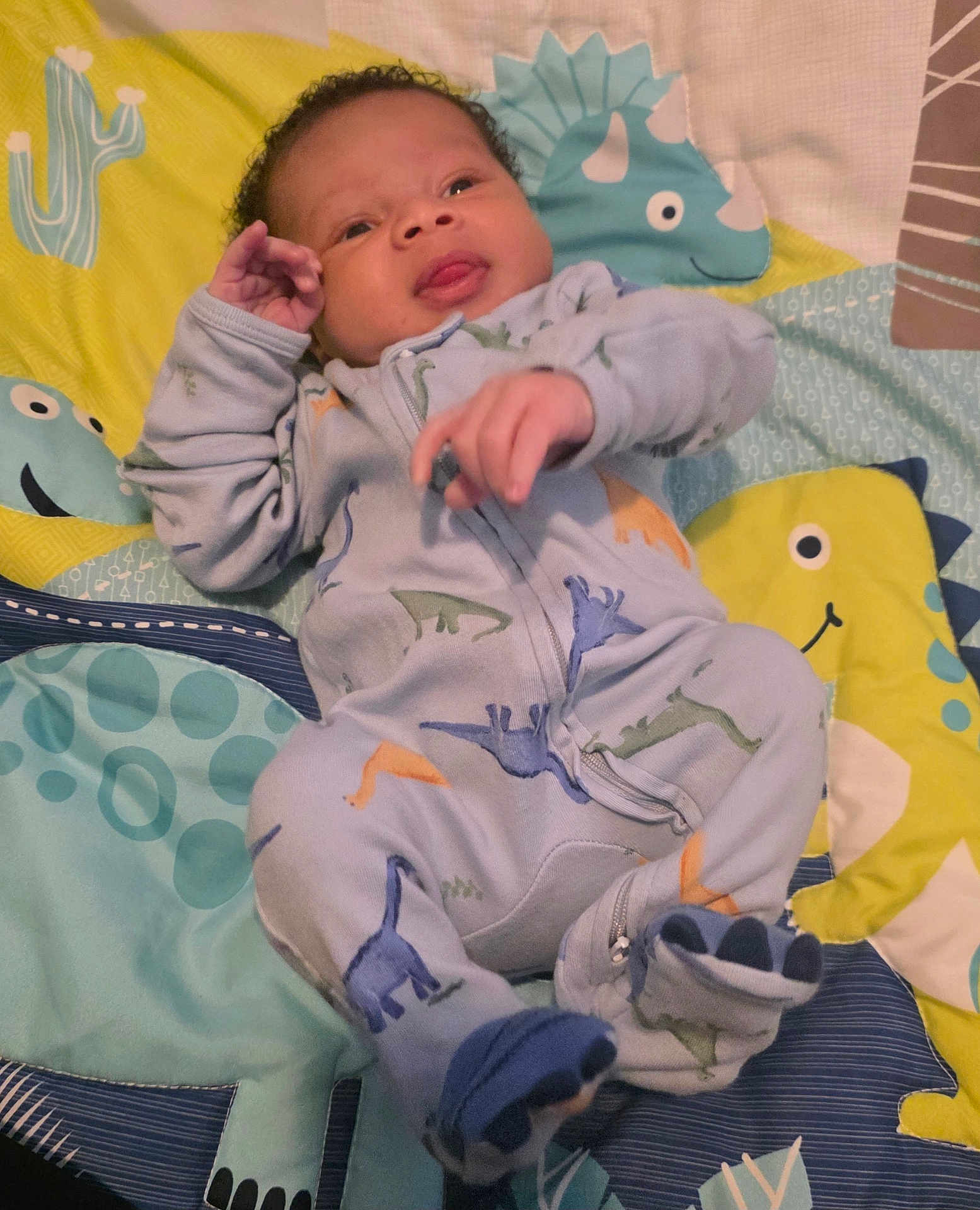 Hakeem is registered to the contest to win money with this photo: baby, infant, onesie, dinosaur, quilt, colorful, cartoon, tongue, cute, smiling, child, sleepwear, fabric, pattern, playful, portrait, indoor, person, soft, lying_down