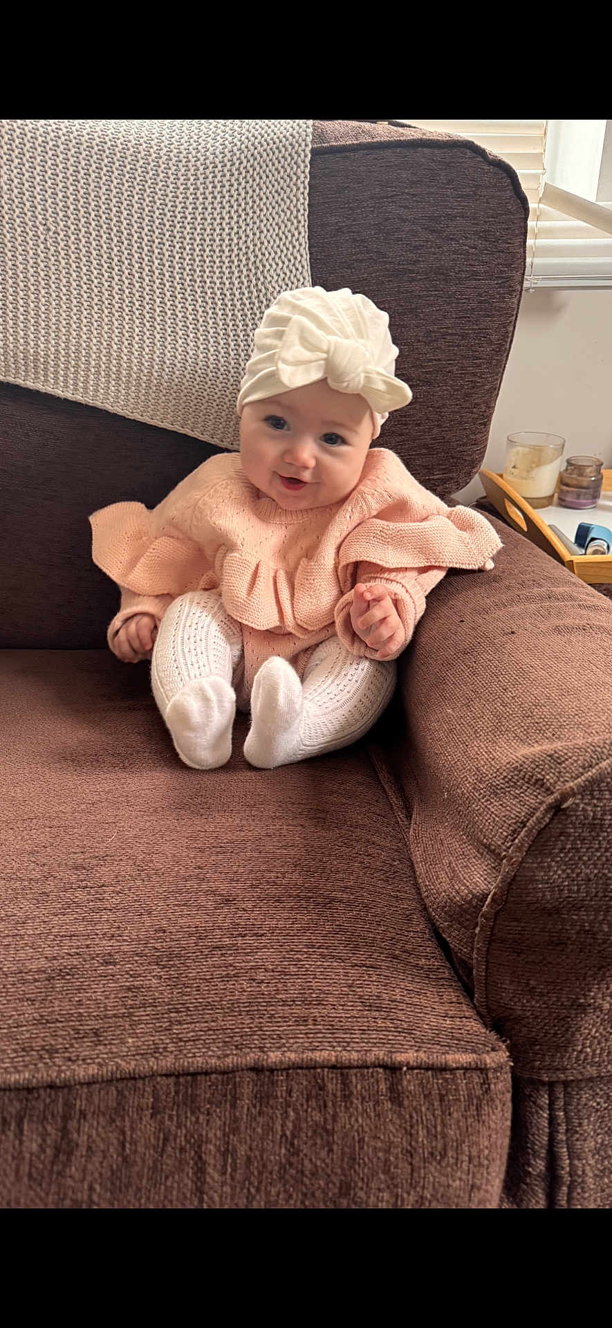 Eleanor is registered to the contest to win money with this photo: baby, infant, child, couch, knitwear, headwrap, bow, pink_sweater, white_leggings, smile, face, indoors, cozy, blanket, seated, furniture, cute, homedecor, window, curtains