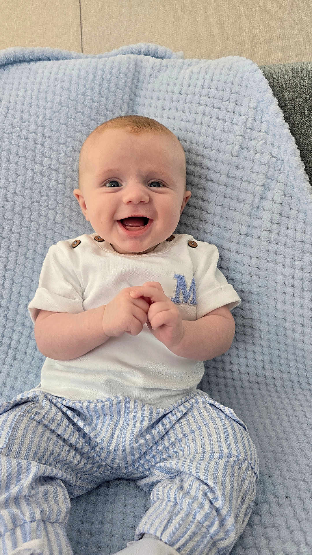 Alfie is registered to the contest to win money with this photo: baby, child, smiling, happy, face, clothing, blue_blanket, striped_pants, white_shirt, sitting, hands, cute, infant, portrait, indoor, soft_texture, light_blue, button_detail, young, person