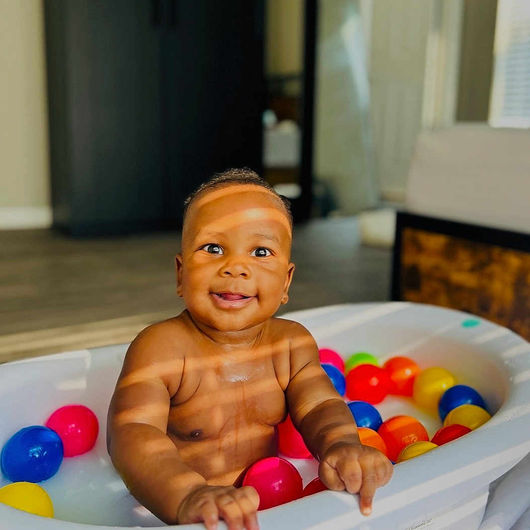 Amiel is registered to the contest to win money with this photo: baby, tub, colorful_balls, indoor, smiling, sunlight, shadow, child, play, happy, skin, face, hand, floor, furniture, window, room, toy, infant, portrait