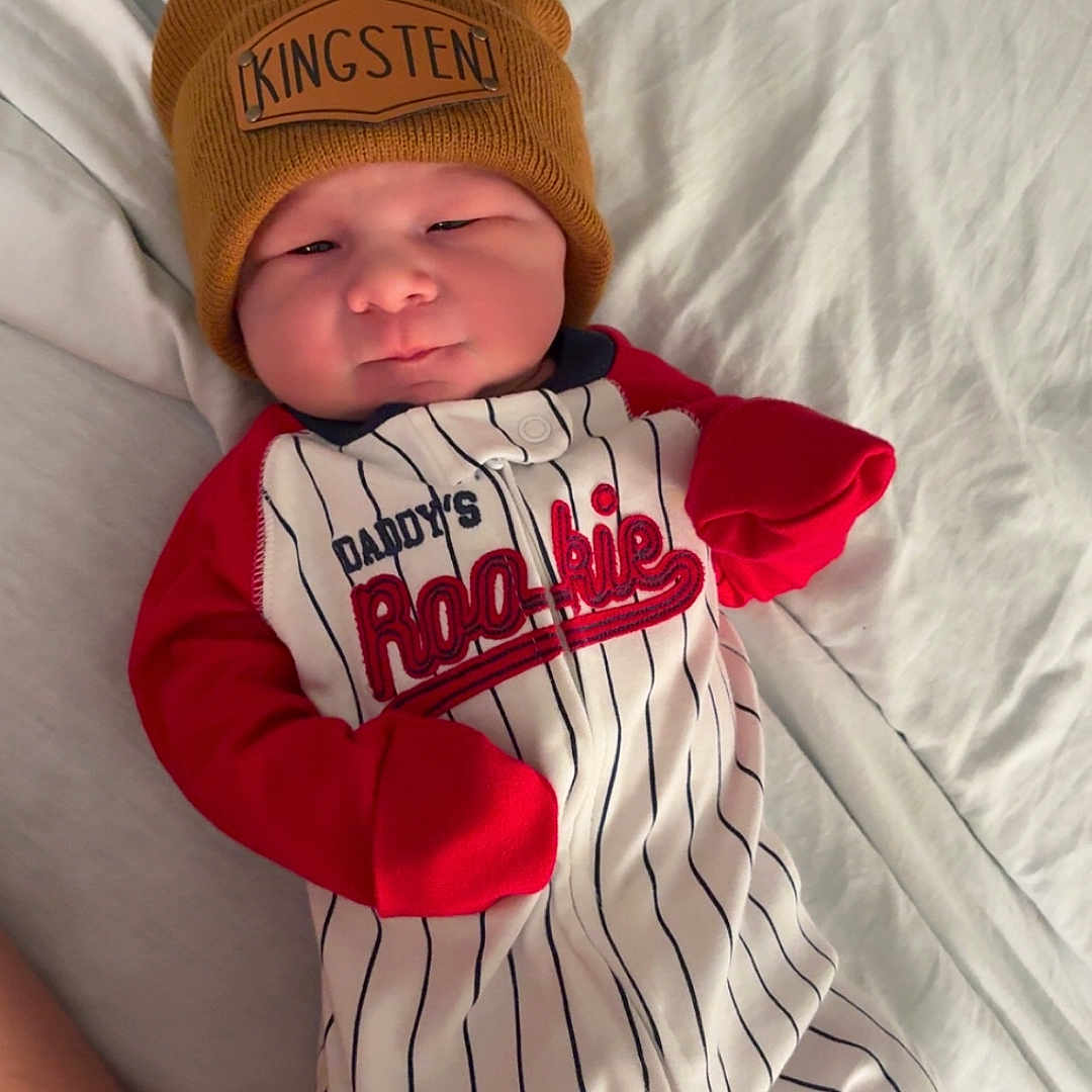 Kingsten joined the competition — help win amazing prizes! baby, beanie, bed, blanket, child, cute, footwear, hat, indoor, infant, onesie, person, portrait, red_sleeves, relaxing, sleepwear, smiling, socks, striped_clothing, young