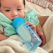 Hannah is registered to the contest to win money with this photo: baby, bottle, feeding, blanket, hand, infant, soft_texture, nursery, sleepy, closeup, person, child, resting, comfort, indoors, cute, toddler, holding, care, parent