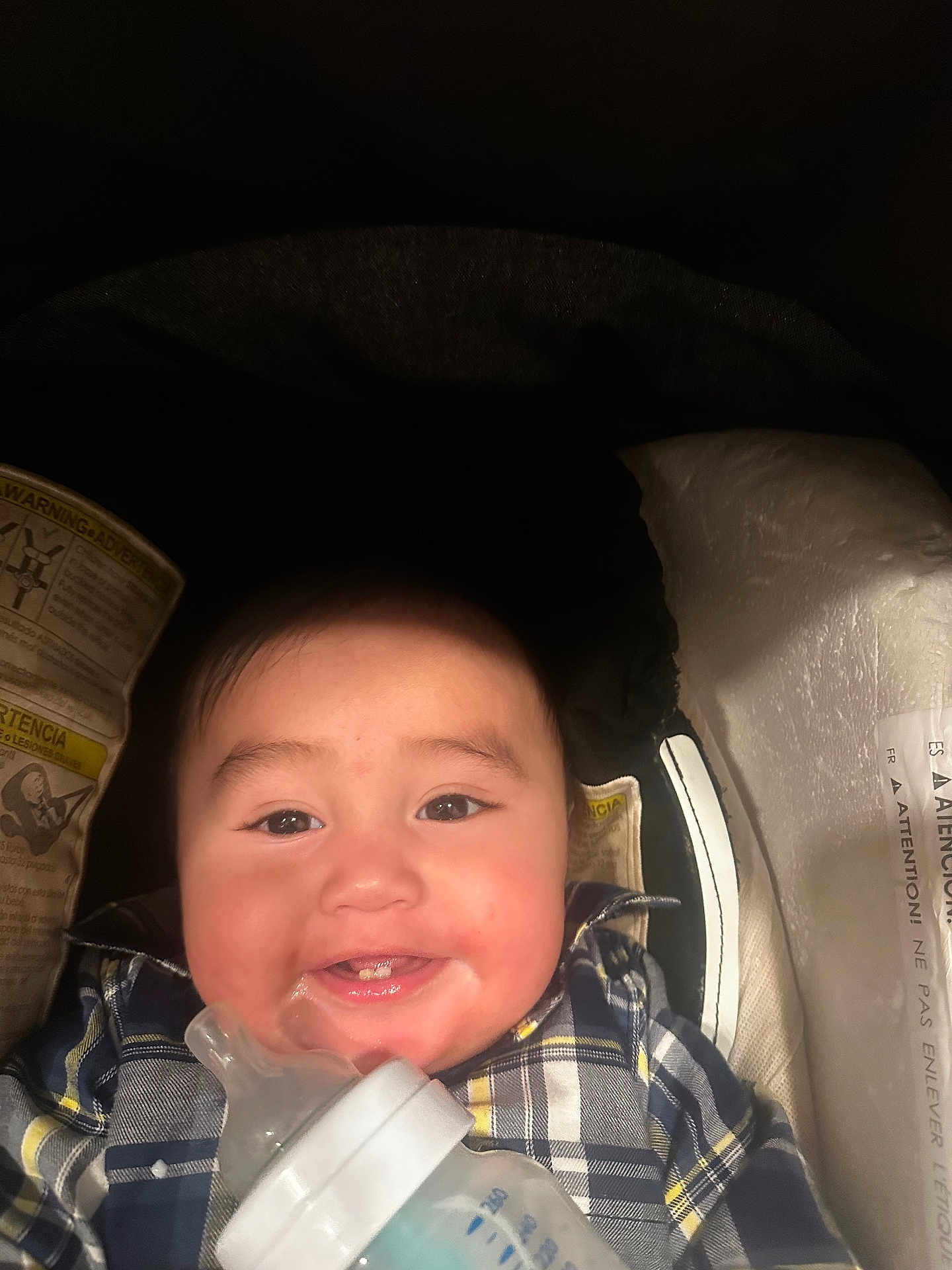 Jose is registered to the contest to win money with this photo: baby, smiling, plaid_shirt, bottle, car_seat, infant, face, child, happy, cute, indoors, person, young, food, feeding, closeup, cheerful, childcare, seatbelt, clothing