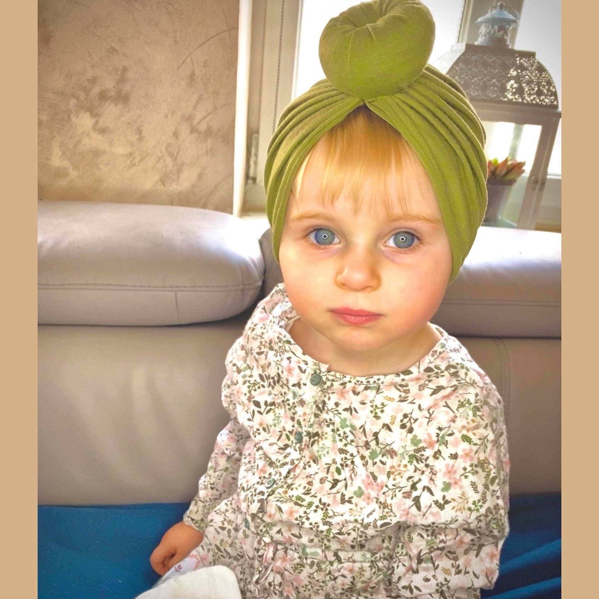 Inès participe au concours pour gagner de l'argent avec cette photo : baby, baby_toddler_clothing, blond, cap, child, comfort, couch, eye, facial_expression, fashion_accessory, flooring, fun, hair, happy, headpiece, iris, person, picture_frame, room, sleeve