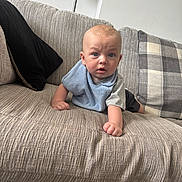George-Anthony joined the competition — help win amazing prizes! baby, infant, blue_eyes, bib, couch, sofa, pillow, plaid_pillow, living_room, furniture, child, person, indoor, curious, expression, skin, head, hand, clothing, home