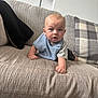 baby, infant, blue_eyes, bib, couch, sofa, pillow, plaid_pillow, living_room, furniture, child, person, indoor, curious, expression, skin, head, hand, clothing, home