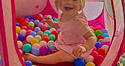 Koura joined the competition — help win amazing prizes! toddler, child, pink_dress, blonde_hair, play_tent, ball_pit, colorful_balls, indoor, smiling, happy, toy, face, sitting, cute, playtime, young_child, fabric, netting, carpet, fun