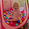 toddler, child, pink_dress, blonde_hair, play_tent, ball_pit, colorful_balls, indoor, smiling, happy, toy, face, sitting, cute, playtime, young_child, fabric, netting, carpet, fun