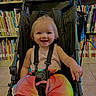 toddler, child, stroller, smiling, rainbow_tutu, indoor, library, bookshelf, books, colorful_clothing, happy, cute, baby, seatbelt, floor_tiles, person, portrait, infant, playful, young_child