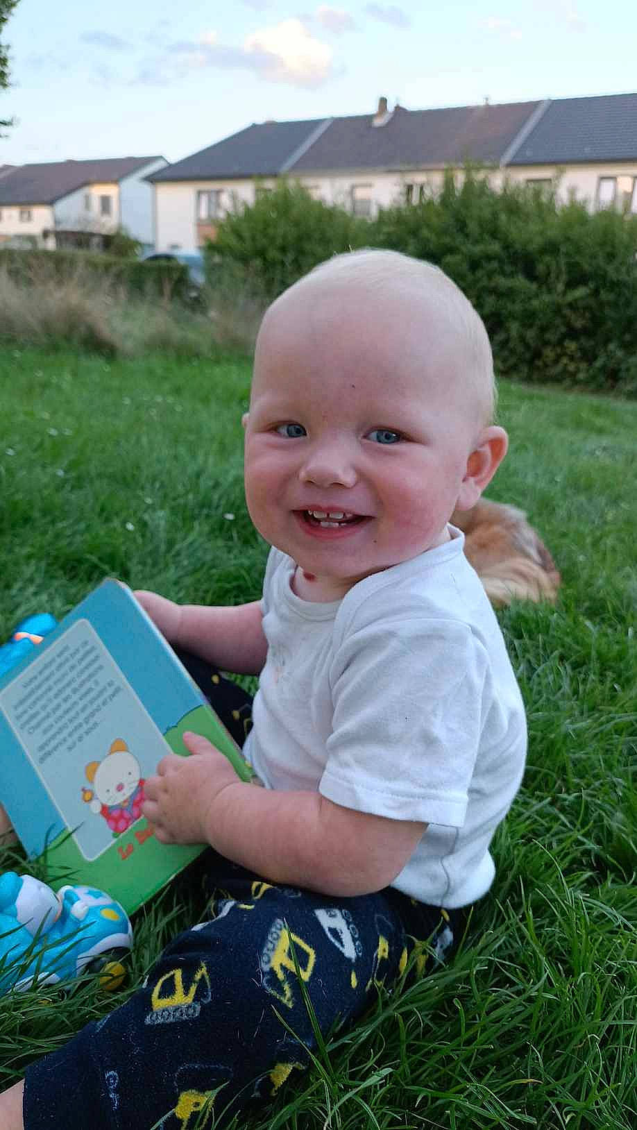 Fabian participe au concours pour gagner de l'argent avec cette photo : baby, baby_toddler_clothing, book, child, fun, garden, grass, grassland, happy, joy, leisure, people_in_nature, person, plant, play, recreation, sitting, sky, smile, t_shirt