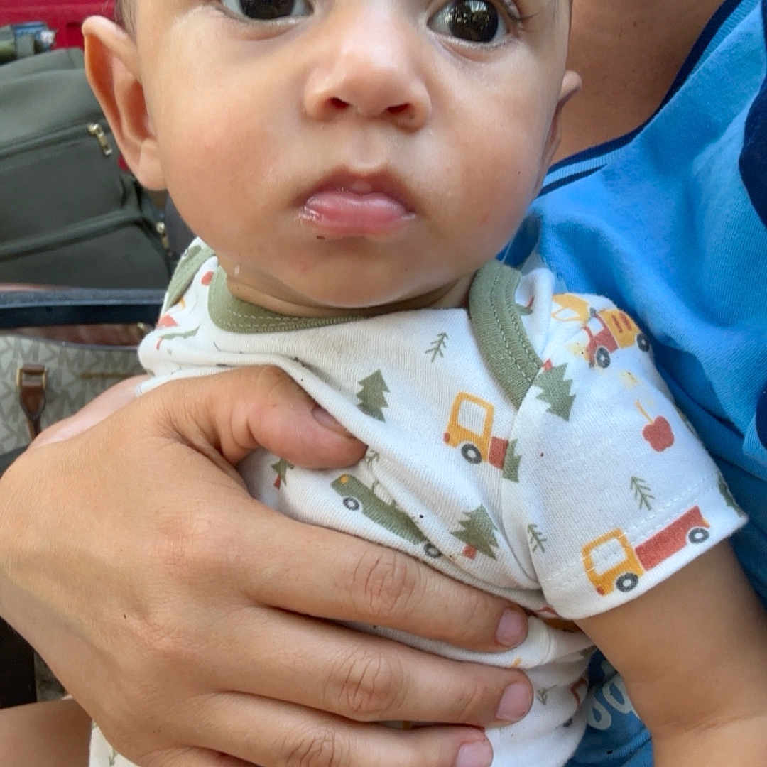 Merlin joined the competition — help win amazing prizes! baby, infant, child, portrait, wide_eyes, serious_expression, sitting, being_held, adult, caregiver, onesie, patterned_clothing, trucks, trees, indoor, close_up, face, hands, family, photography
