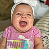baby, child, smiling, happy, headband, bow, pink_shirt, puma_logo, indoor, cushion, pattern, cheeks, tongue, person, portrait, cute, infant, clothing, seated, closeup