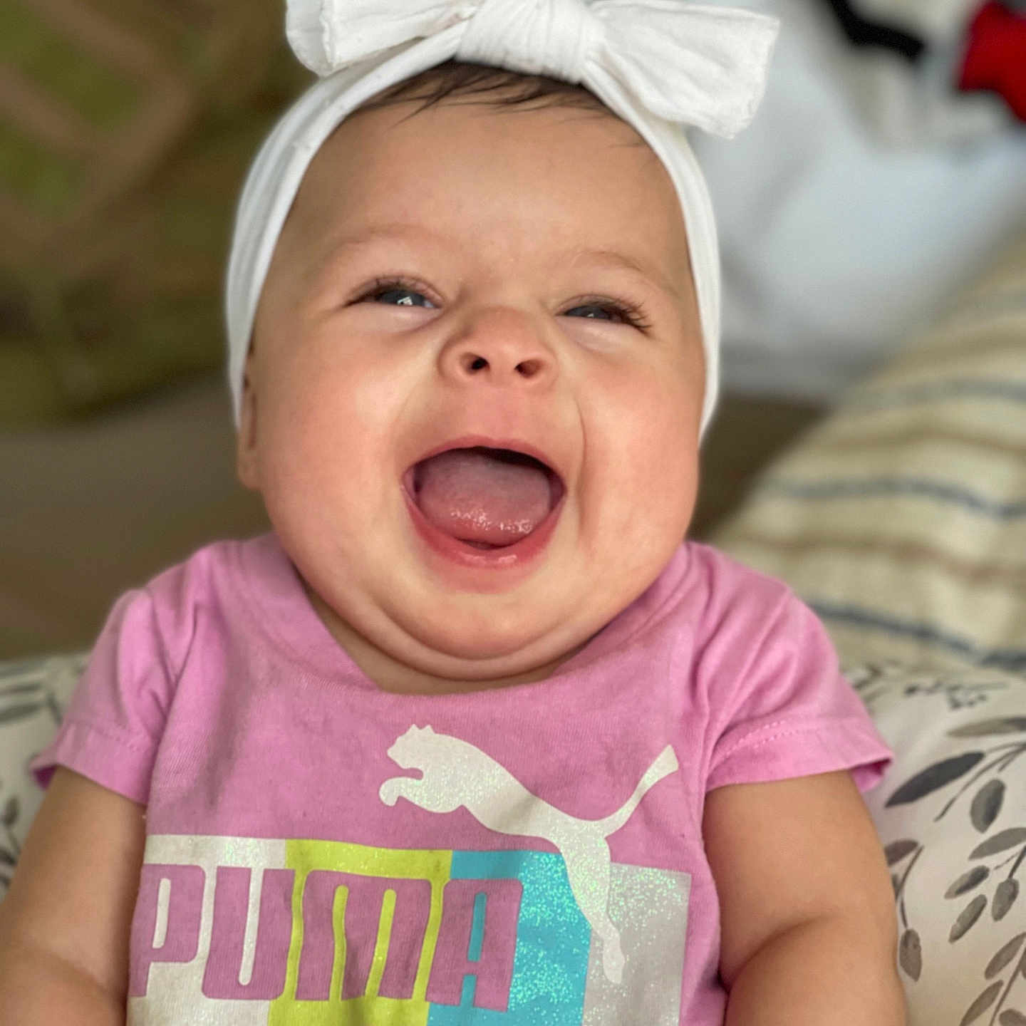 Kemiah joined the competition — help win amazing prizes! baby, child, smiling, happy, headband, bow, pink_shirt, puma_logo, indoor, cushion, pattern, cheeks, tongue, person, portrait, cute, infant, clothing, seated, closeup