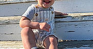 Kayson joined the competition — help win amazing prizes! toddler, child, smiling, sitting, steps, outdoor, sunlight, blue_sky, overalls, short_sleeves, shoes, sneakers, hairstyle, mohawk, wood, weathered, happy, person, casual, daytime