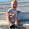 toddler, child, smiling, sitting, steps, outdoor, sunlight, blue_sky, overalls, short_sleeves, shoes, sneakers, hairstyle, mohawk, wood, weathered, happy, person, casual, daytime