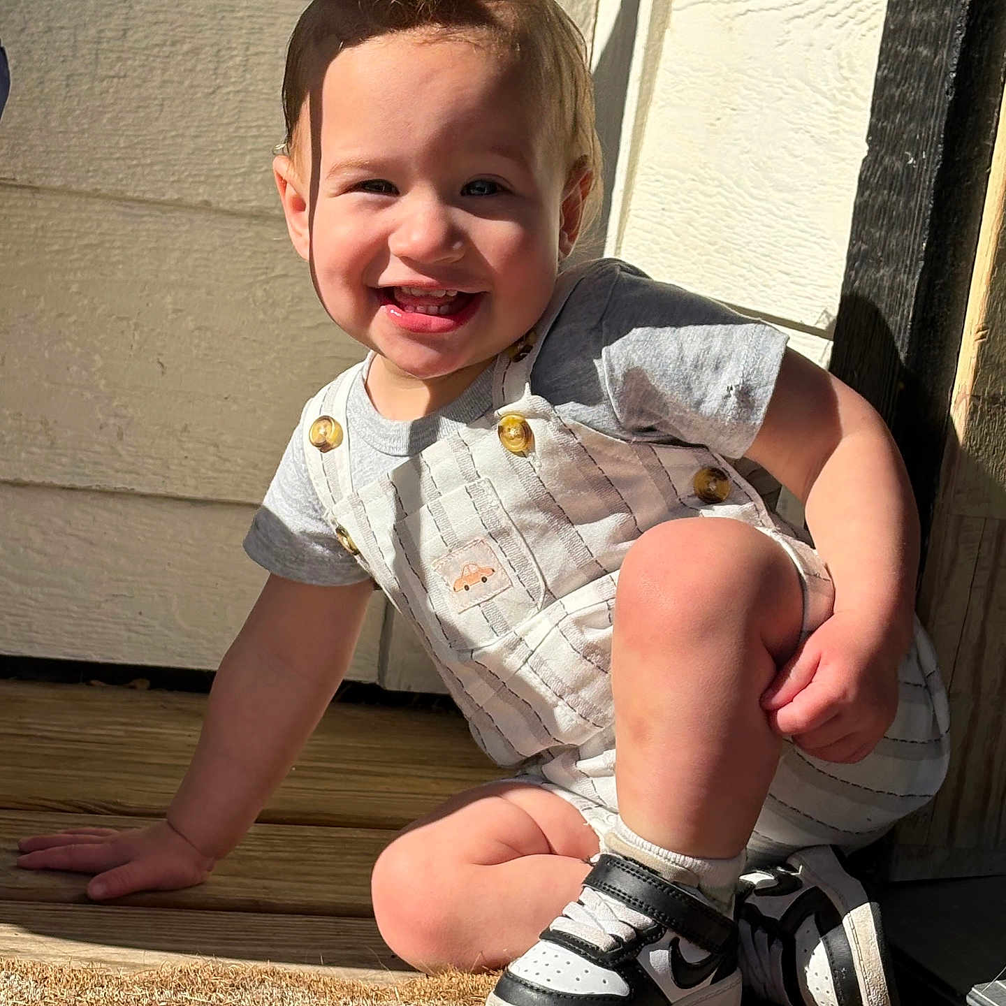 Kayson joined the competition — help win amazing prizes! toddler, child, smiling, sneakers, outdoor, sunlight, shadow, wood_floor, striped_overall, golden_buttons, crouching, happy, portrait, person, short_sleeve, door, wall, playful, casual_clothing, daylight